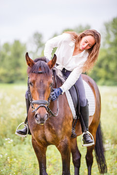 Young rider girl bent toward horse for complimenting it