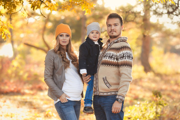 Fototapeta premium Young happy family have fun and walking in the autumn park. Pregnant woman with husband and little son