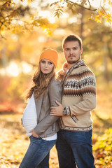 Young happy family have fun and walking in the autumn park. Pregnant woman with husband 