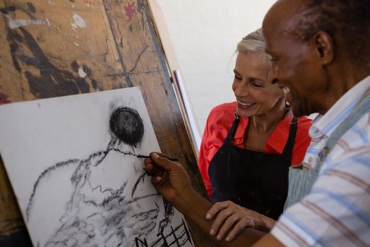 Senior woman assisting man while painting on paper