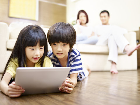 asian children lying on floor using digital tablet while parents watching in the background. 