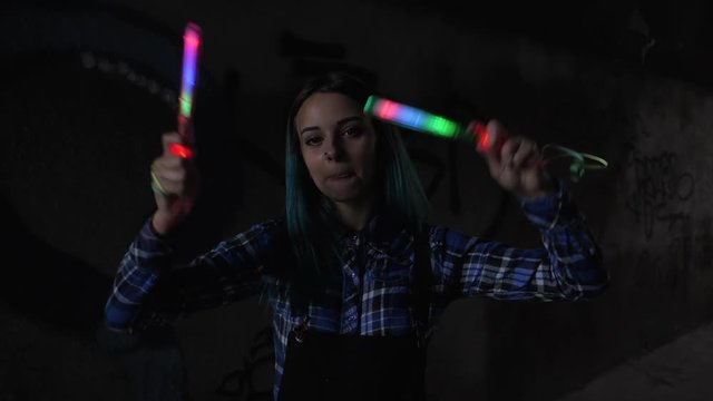 SLOW MOTION: Portrait of model girl with blue hair looks with colorful wand in hands. Close up. Beautiful young teenage in city tunnel having fun with magic flashing sticks