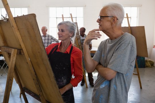 Senior adult looking at woman painting on easel