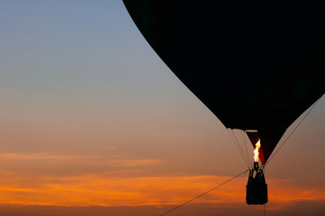 Silhouette of people flying in balloon high in sky at sunset on orange sky background. Romantic recreation. Hot air balls competition. Autumn ballooning festival. Airship fuel. Travel and tourism.