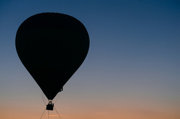 Silhouette of people flying in balloon high in sky at sunset on orange sky background. Romantic recreation. Hot air balls competition. Autumn ballooning festival. Airship fuel. Travel and tourism.