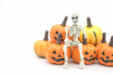 Halloween Concept. Skeleton miniature figure model  sitting on mini Jack o' lantern pumpkin toys on white background.