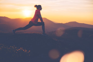Silhouette of athletic girl doing stretching after a great jog in the mountains at sunset. Sport...