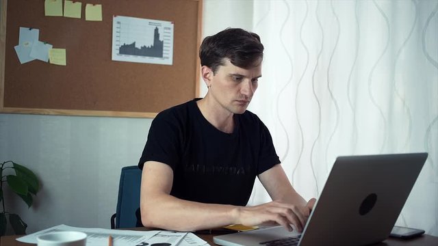 Freelancer using laptop computer in the home office. A board with stickers and graphs on the wall behind