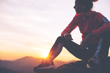 Silhouette of athletic girl resting after a hard training in the mountains at sunset. Sport tight clothes.