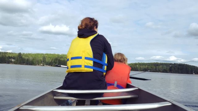 A little girl holds a fishing rod while her mother paddles in the waters of Georgian Bay, Ontario. Rear view shot.