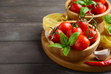 Fresh red cherry tomatoes with raw pasta, basil, chili pepper and garlic for Italian food, selective focus, copy space.