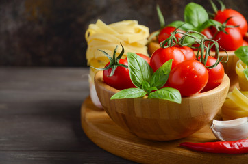 Fresh red cherry tomatoes with raw pasta, basil, chili pepper and garlic for Italian food, selective focus, copy space.