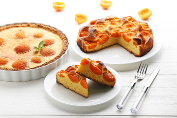 Slices of apricot pie with fruits on white wooden table