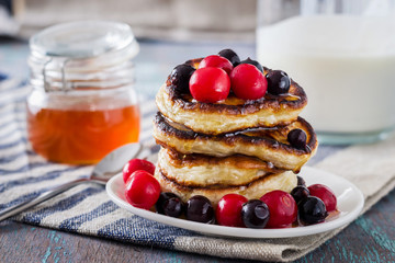 white plate full of pancakes with berries on a wooden background