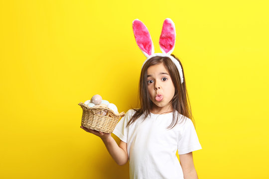 Beautiful little girl with rabbit ears and easter eggs on yellow background