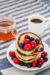 white plate full of pancakes with berries and honey on a wooden background