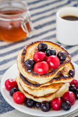 white plate full of pancakes with berries and honey on a wooden background