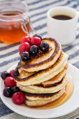 white plate full of pancakes with berries on a wooden background