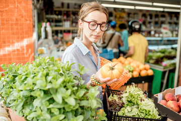 Young woman choosing a fresh tomato standing with basket at the food market in France