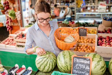 Young woman choosing a fresh watermelon standing with basket at the food market in France