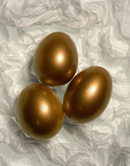 Three golden eggs on white tissue paper