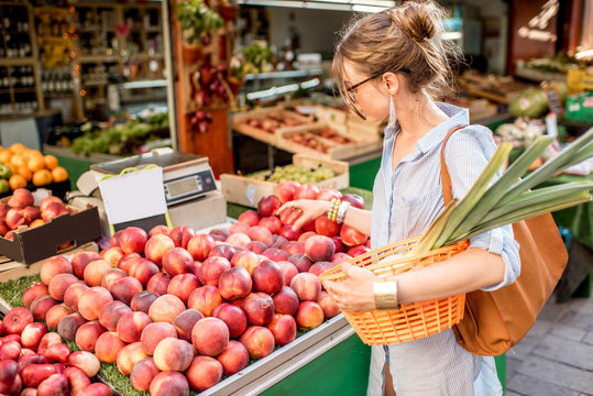 Young Woman Choosing A Fresh Peach Standing With Basket At The Food Market In France