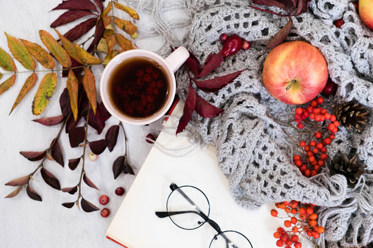 Cozy winter still life: cup of hot coffee and opened book. Cup of tea with open book and bunch of red rowan on wooden background, vintage picture style. Autumn, fall leaves, Flat lay, top view.