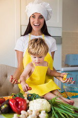 The young cook mother standing with her little son in the kitchen and smiling and cooking some food
