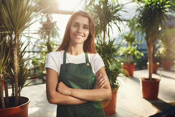 Naklejka premium Portrait of happy gardener in greenhouse looking at camera smiling. Light leak from behind.