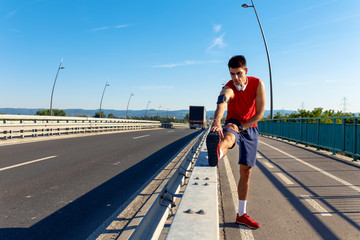 Young athlete man stretching his muscles before running on bridge on sunny day.