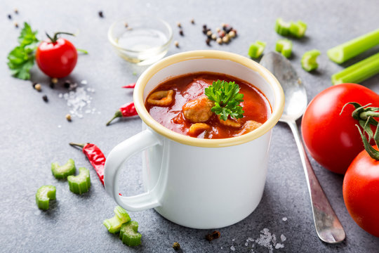 White enamel mug with delicious homemade tomato soup with meatballs and pasta. Healthy food concept.