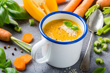 White enamel mug with delicious homemade carrot soup with meat sesame seeds and basil. Healthy food concept.