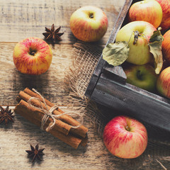 Box with ripe apples and cinnamom on wooden background