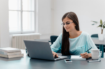 Portrait of smiling businesswoman with laptop writes on a document at her office