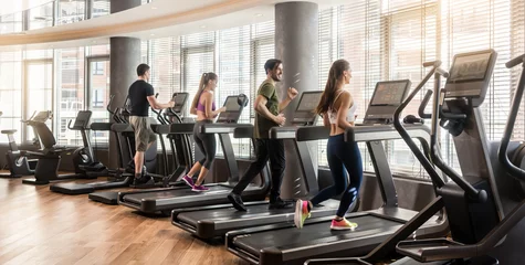 Foto auf Acrylglas Fitness Gruppe von vier Personen, Männer und Frauen, die in einem modernen und leuchtenden Fitnessstudio auf Laufbändern laufen