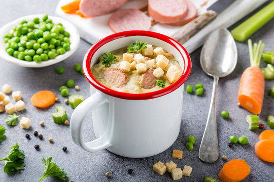 White enamel mug with delicious homemade pea soup with sausage and croutons. Healthy food concept.