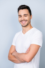 Obraz premium Close up portrait of successful young stylish bearded brunet in white t shirt, standing on light grey background with crossed hands
