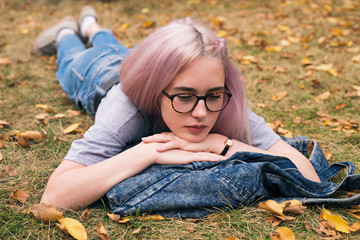 Pink-haired girl in glasses lying on denim rucksack with arms under chin