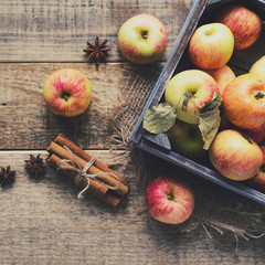 Box with ripe apples and cinnamom on wooden background