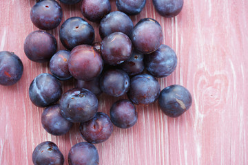 Ripe plums on a pink wooden background