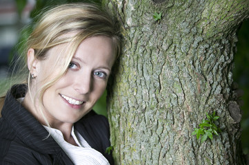 Blonde Frau lächelnd an einem Baum gelehnt