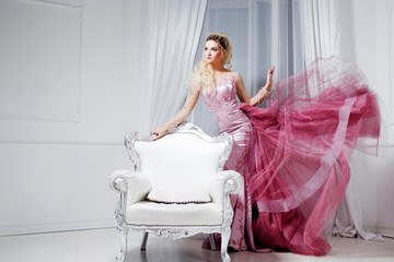 Young beautiful woman in a luxurious pink dress, in interior near the white chairs