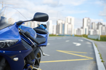 Transport, urban lifestyle, transportation, speed, freedom, traveling, driving and extreme sports concept. Detailed front view of blue motorcycle parked on road with skyscrapers in background