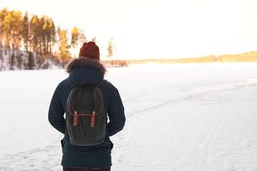 Fashionable hipster traveler with backpack wearing red hat and coat walking alone in winter snowy...
