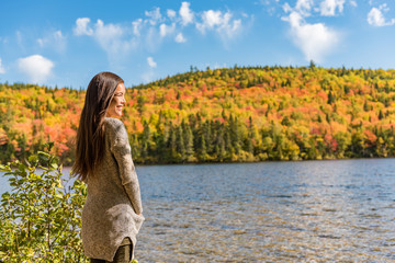 Autumn girl at forest lake enjoying watching nature view. Autumn forest colors woman relaxing at countryside vacation getaway. Outdoor autumn landscape tranquility.
