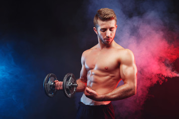 Young ripped man bodybuilder with perfect abs, shoulders,biceps, triceps and chest working out with a dumbbell, studio shoot