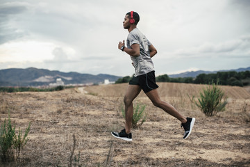 African american man using headphones running on a field at evening.
