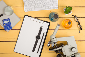 Education and science concept - microscope, book, magnifying glass, calculator, watch, blank clipboard, computer keyboard, eyeglasses and chemical liquids