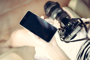 Female hand holding DSLR camera and smartphone, light background. Close up top view mockup screen