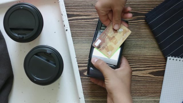 Top view shot of a man using mobile paypass technology buys with coffee to go in acafe